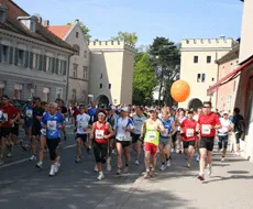 Un gruppo di corridori in abbigliamento sportivo corre lungo una strada cittadina, alcuni con un palloncino arancione.