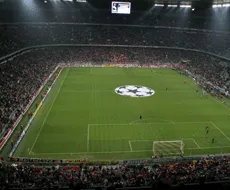 Un stadio di calcio con uno schermo grande e un logo al centro del campo da gioco.