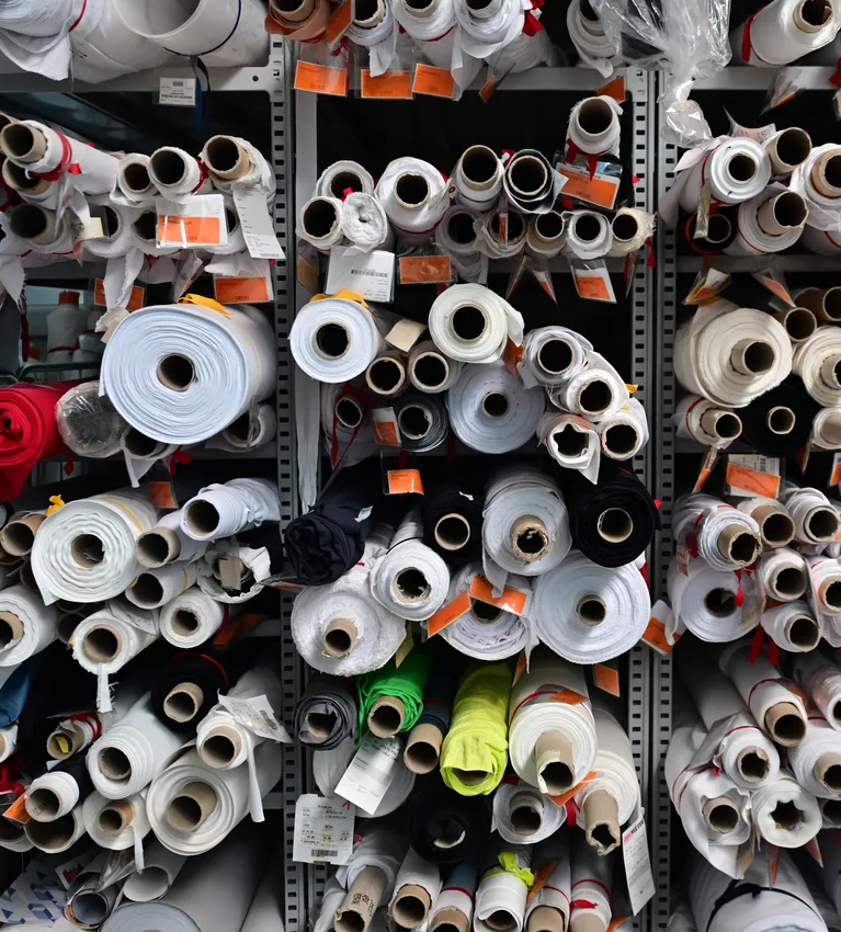 Scaffali pieni di rotoli di tessuto di vari colori e dimensioni, immagazzinati per la produzione di abbigliamento sportivo su misura.