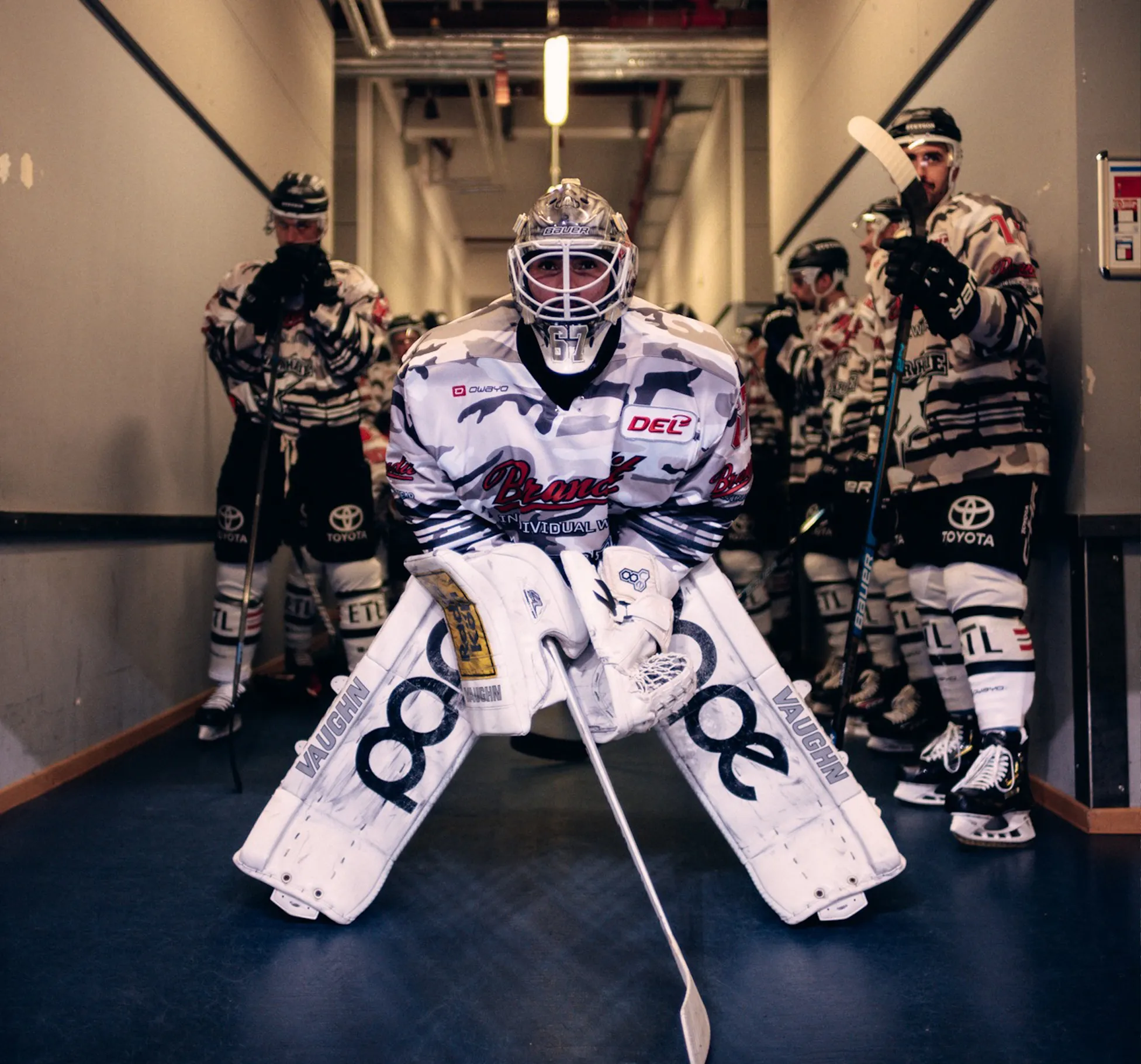 Un portiere di hockey in un uniforme vistoso è pronto, mentre altri giocatori aspettano dietro di lui.