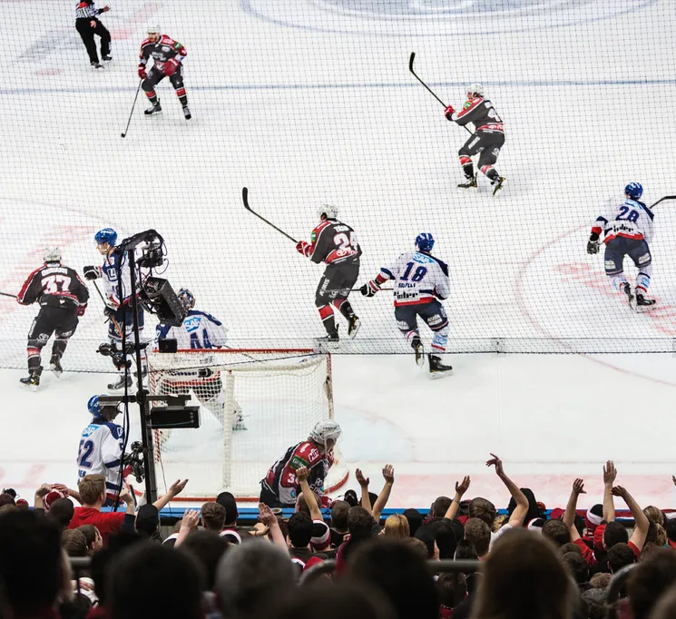 Una scena dinamica di hockey su ghiaccio con giocatori in azione sul ghiaccio e una folla in festa sullo sfondo.