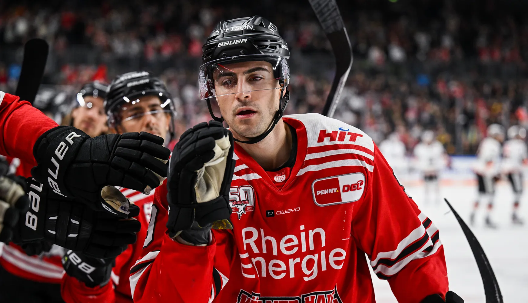 Un giocatore di hockey in una maglia rossa con strisce bianche e guanti, che reagisce durante la partita.
