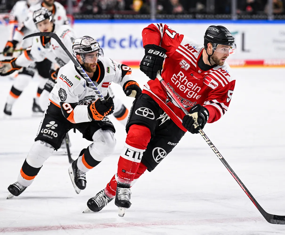 Due giocatori di hockey su ghiaccio sul ghiaccio, uno in maglia rossa e l'altro in maglia bianca con accenti arancioni.