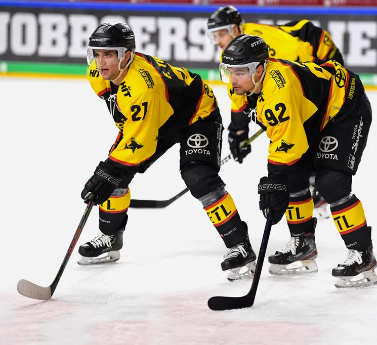 Giocatori di hockey su ghiaccio con maglie gialle e nere con i numeri 21 e 92 sul ghiaccio, che tengono i loro bastoni.