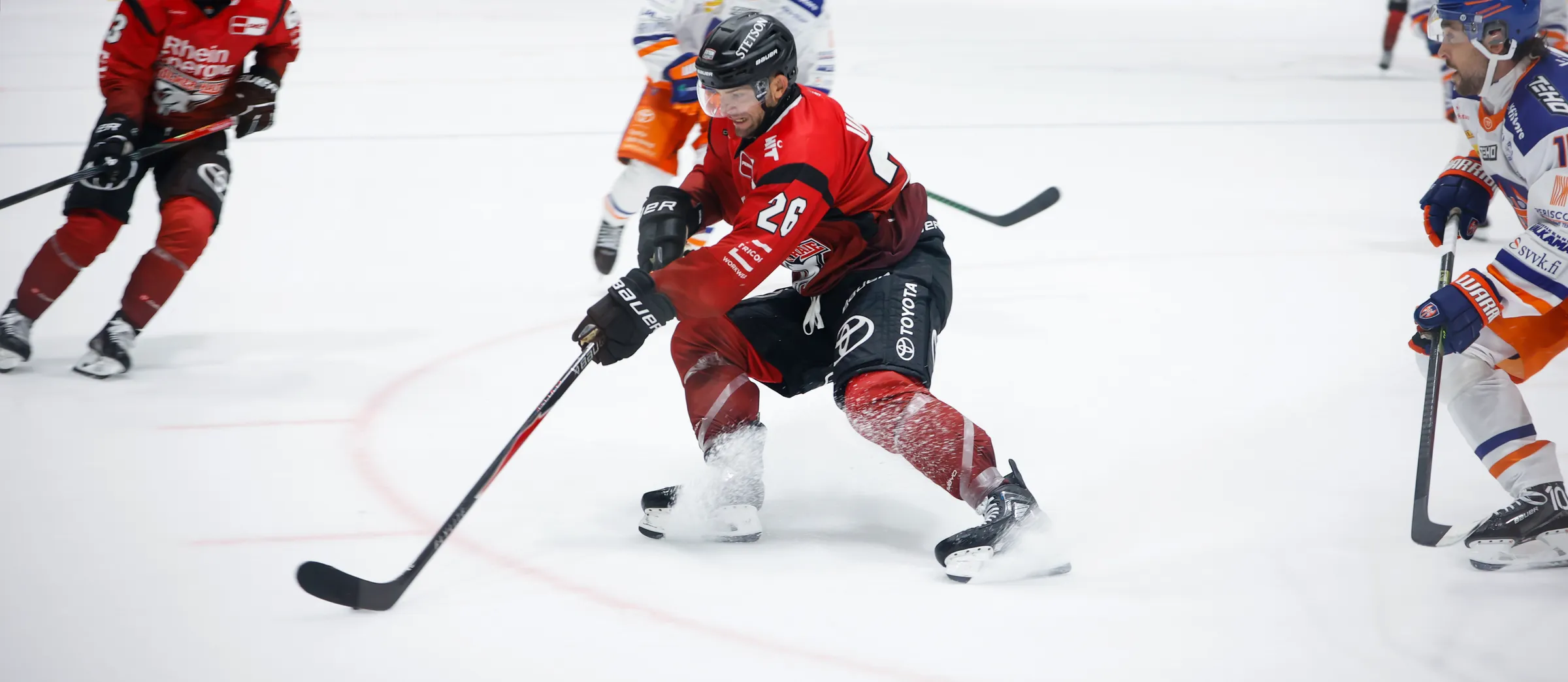 Un giocatore di hockey su ghiaccio in abbigliamento sportivo rosso sta dribblando il puck sul ghiaccio.