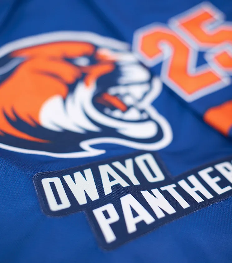 Primo piano di una maglia sportiva blu con un logo di pantera arancione e la scritta 'OWAYO PANTHERS' in lettere bianche su una toppa scura.