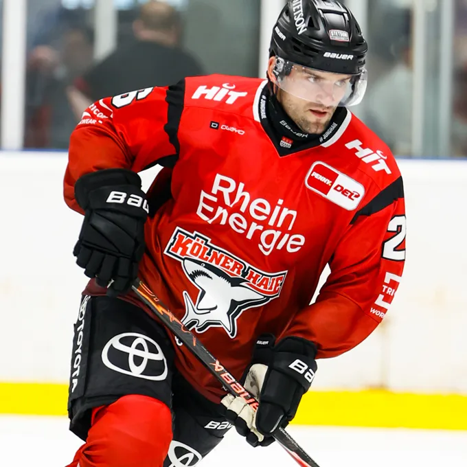 Un giocatore di hockey su ghiaccio con una maglia rossa con il logo di Rhein Energie e Kölner Haie, sul ghiaccio.