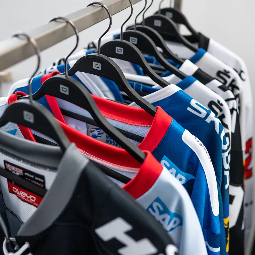 Una fila di diverse maglie sportive colorate appese a una gruccia.
