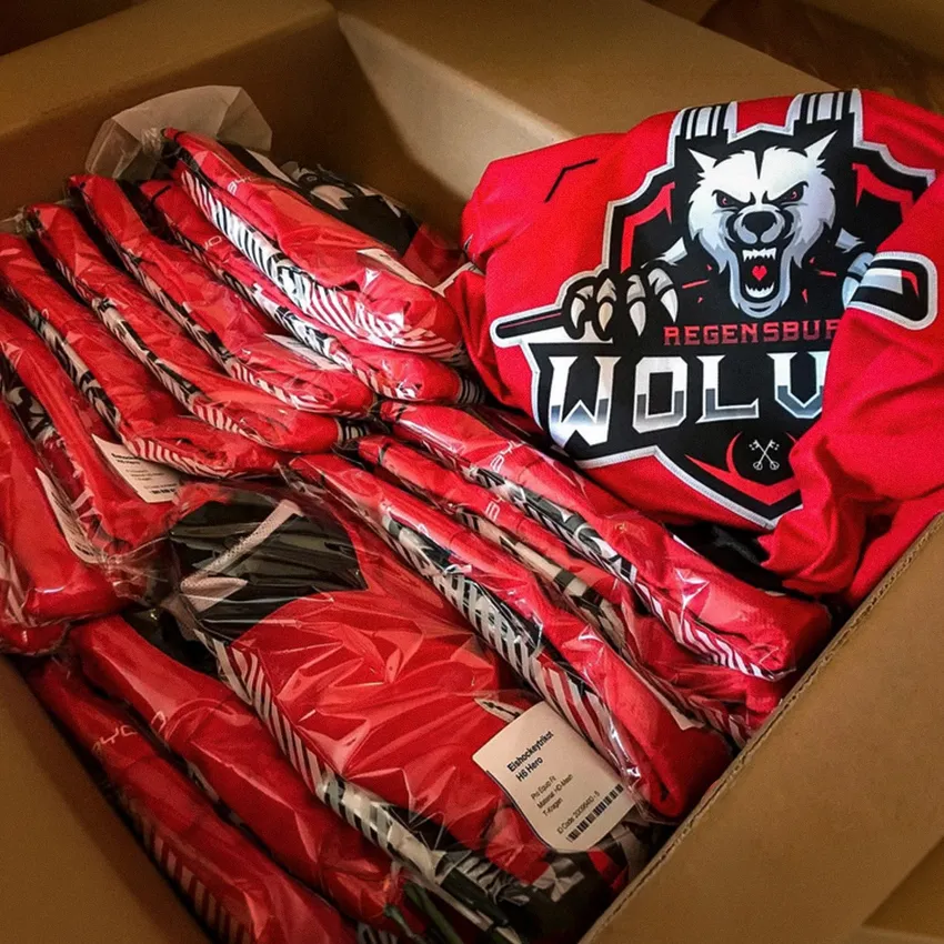 Una scatola piena di abbigliamento sportivo rosso con un logo di lupo e vari capi avvolti in imballaggi trasparenti.