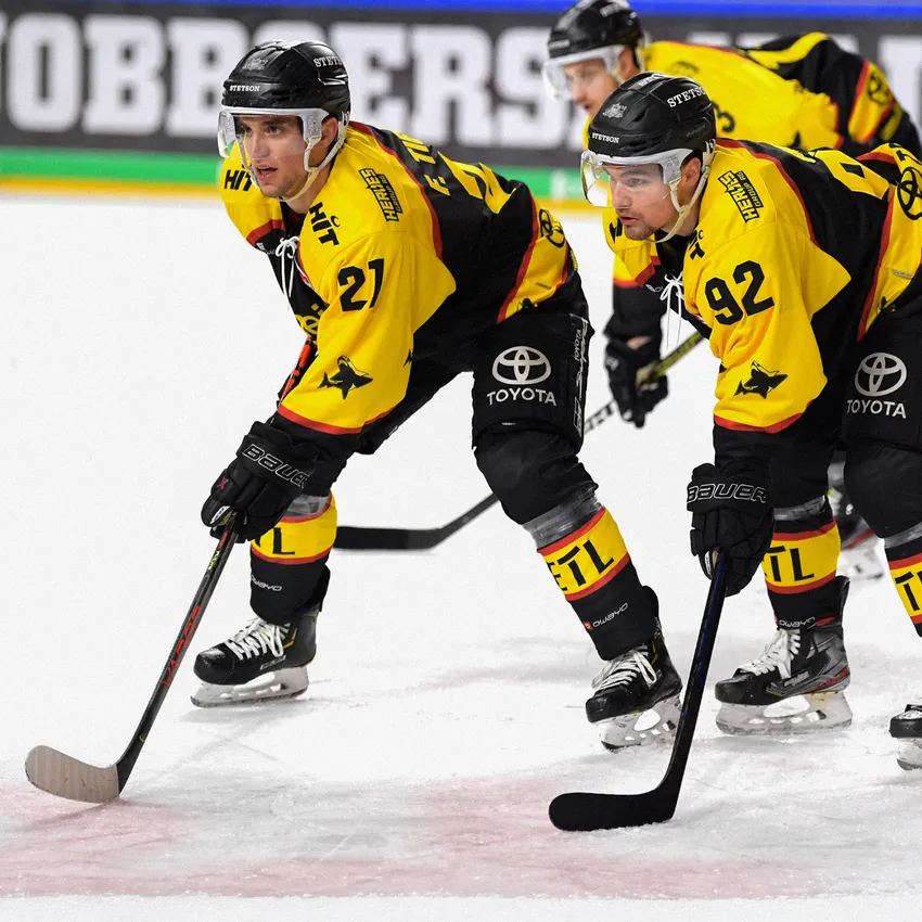 Due giocatori di hockey su ghiaccio in maglie giallo e nere sono in piedi sul ghiaccio, pronti per la partita.