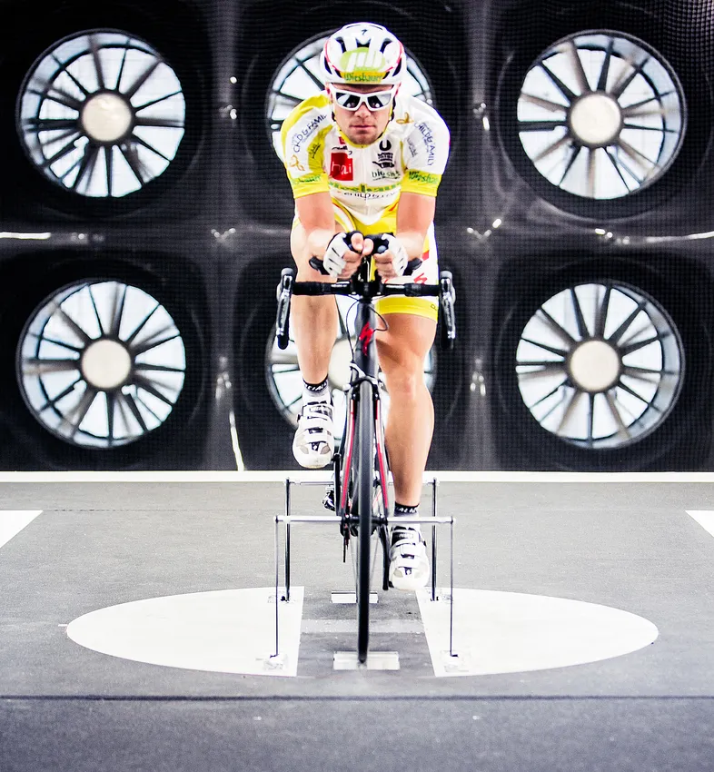Un ciclista in posizione aerodinamica su una bicicletta in un tunnel del vento, per testare le prestazioni di abbigliamento sportivo su misura.