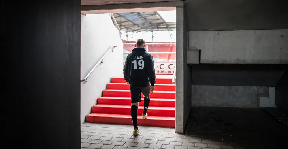 Un atleta in un felpa nera con il numero 19 e pantaloni corti neri che sale una scala rossa in uno stadio.