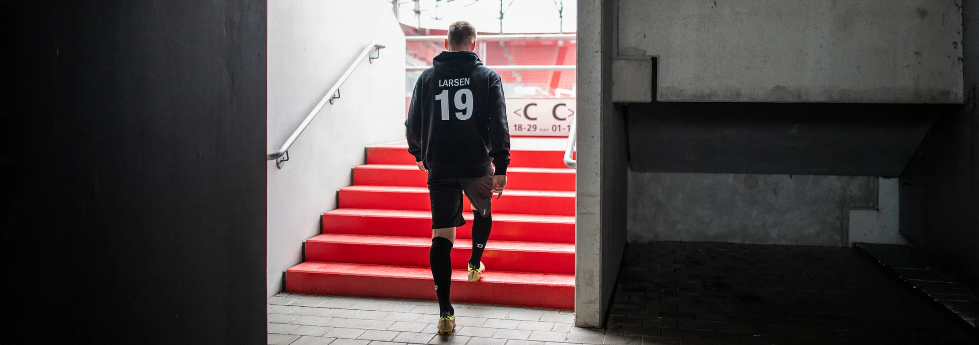Un atleta scende le scale indossando un abbigliamento sportivo, diretto verso il campo.
