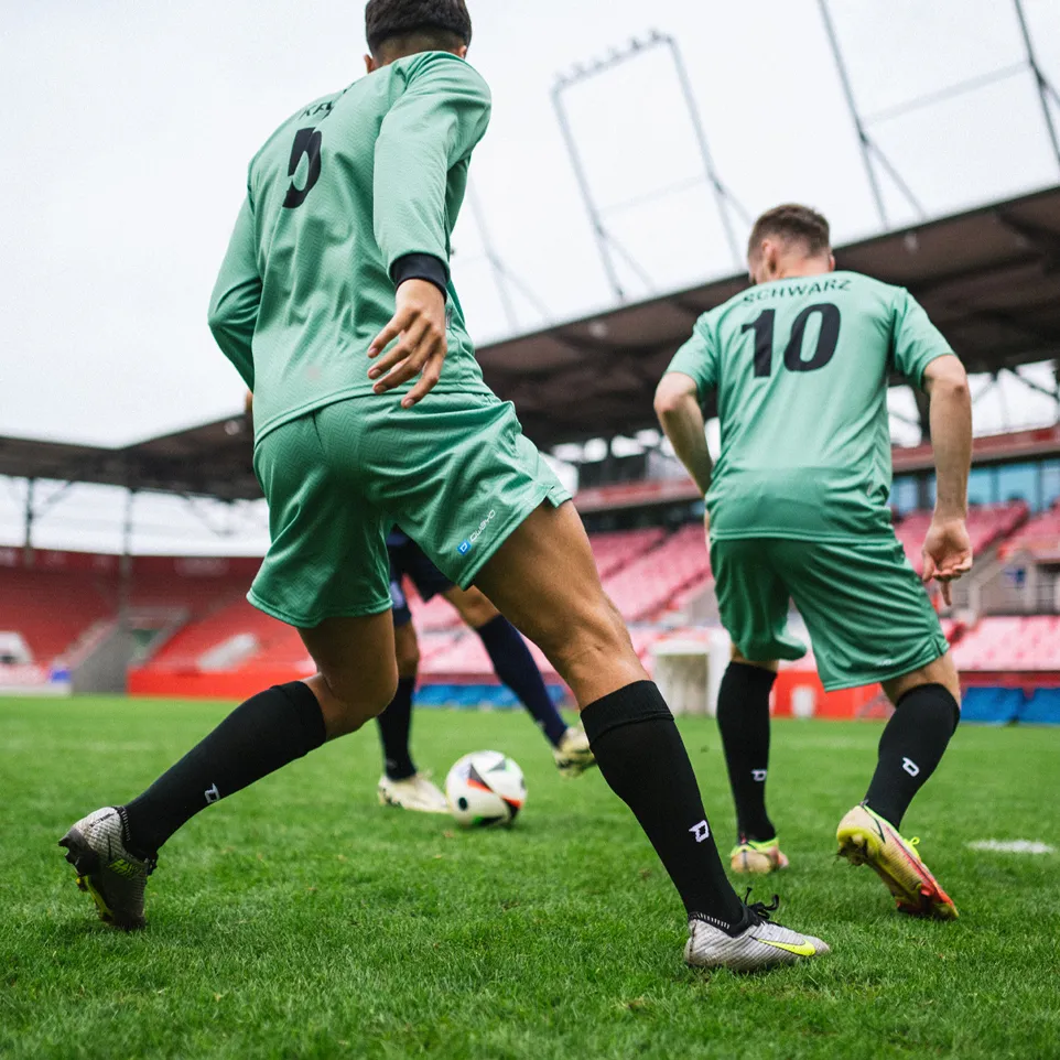 Due calciatori in maglie verdi e calze nere che giocano attivamente su un campo d'erba in uno stadio.