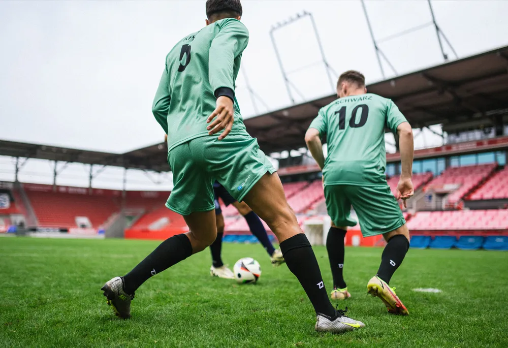 Due calciatori in magliette verdi e calze nere che giocano su un campo in erba.