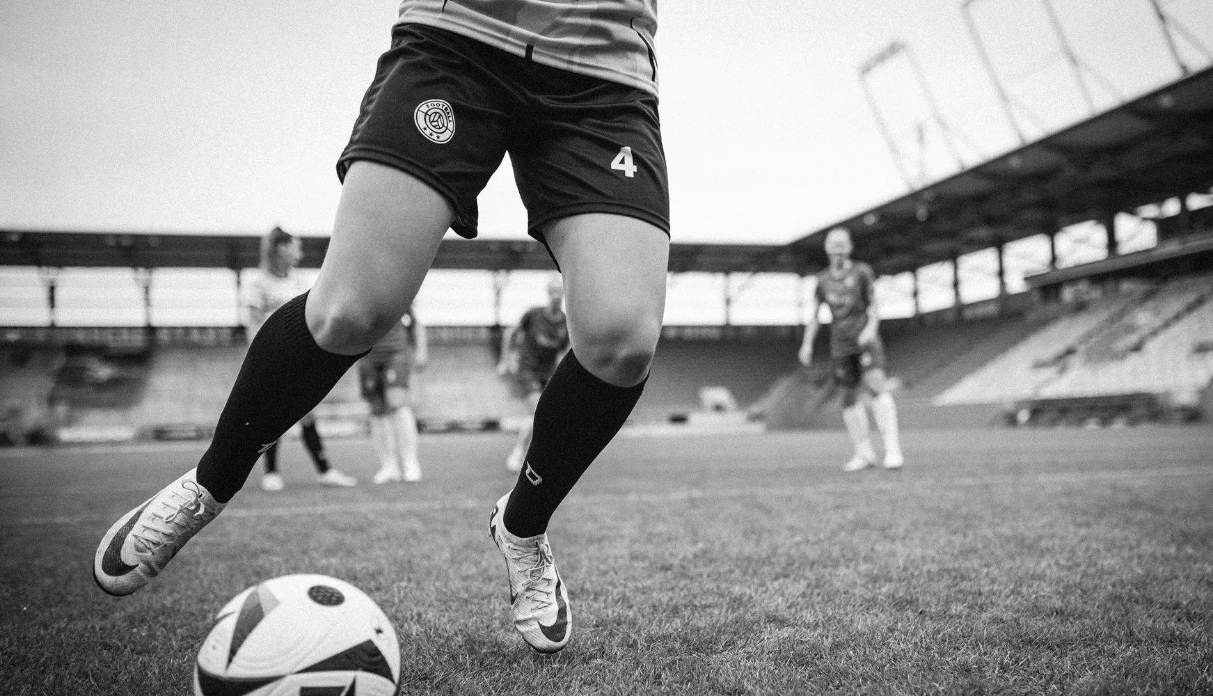Una giocatrice in pantaloni corti da calcio e calze lunghe sta calciando un pallone su un campo da calcio.