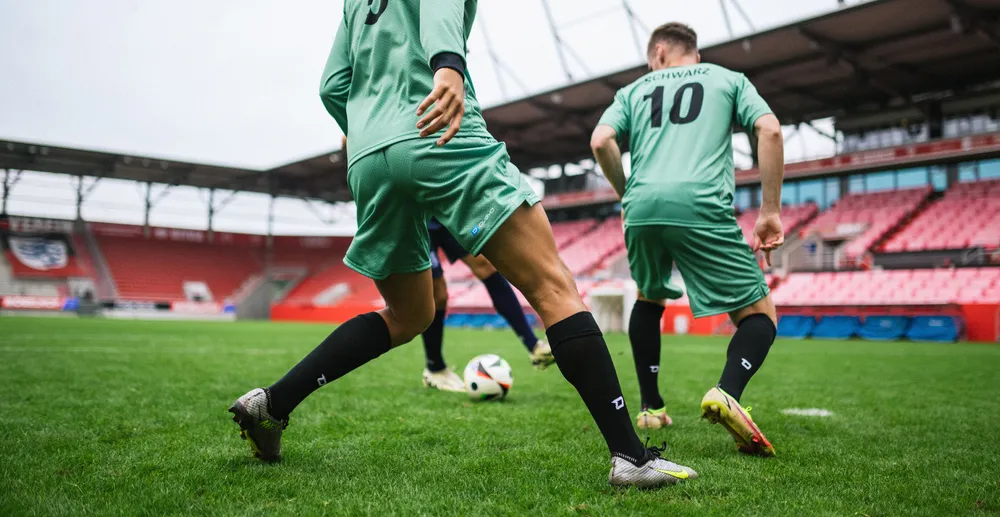 Due calciatori in magliette verde chiaro e calze nere che si allenano su un campo in erba in uno stadio.