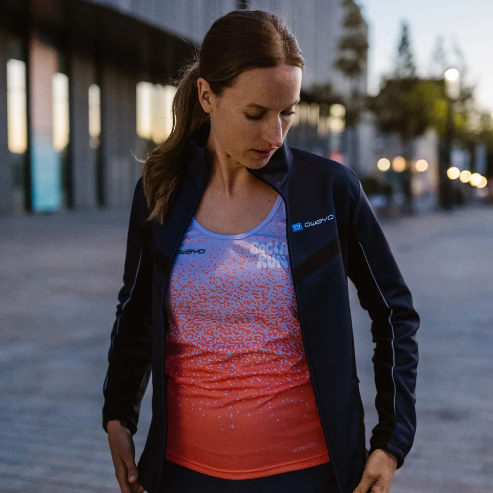 Una donna indossa una giacca sportiva e una maglietta senza maniche colorata con un design moderno mentre si trova su una strada urbana.