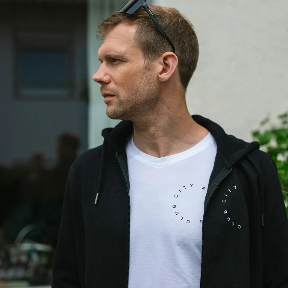 Un uomo indossa un hoodie nero sopra una maglietta bianca con una stampa circolare.