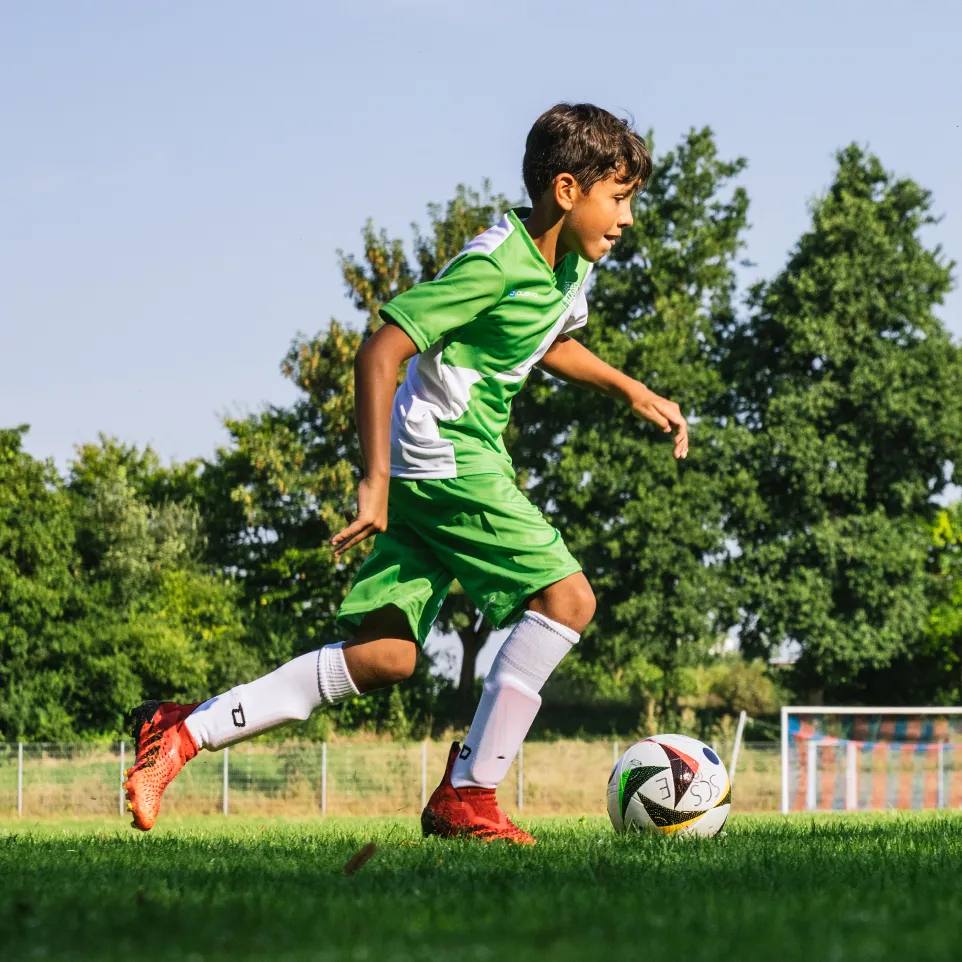 Un giovane calciatore in abbigliamento sportivo verde e bianco corre su un campo da calcio.