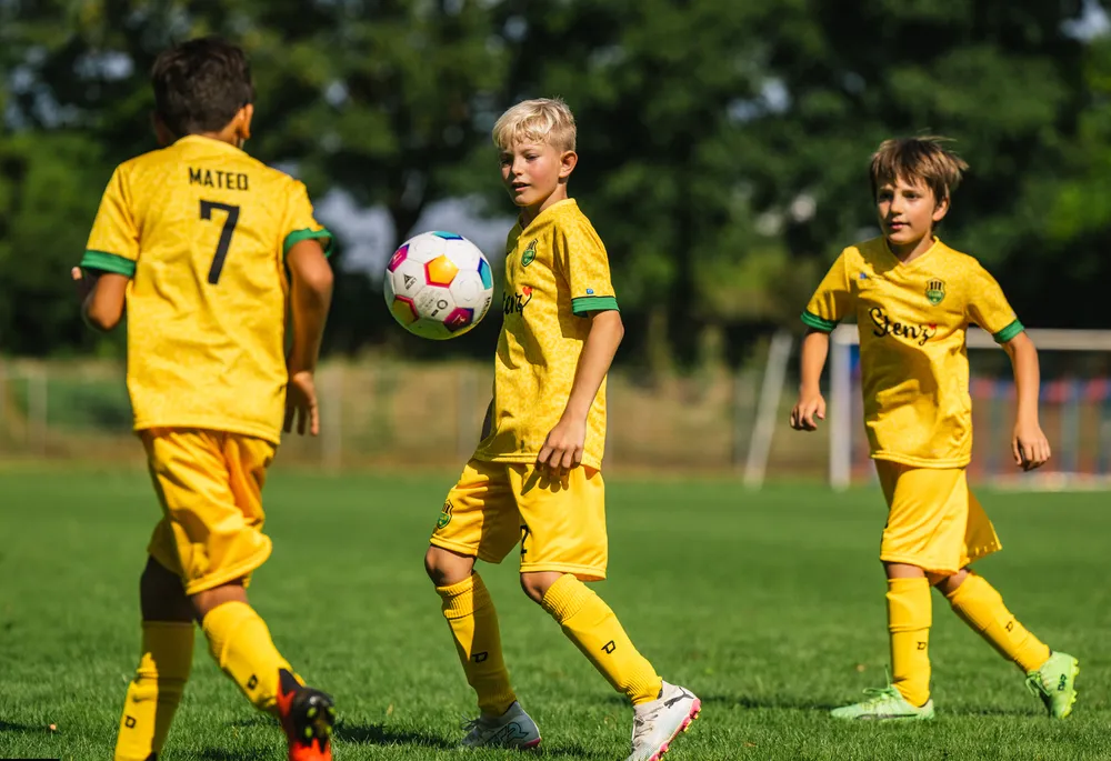 Tre bambini in magliette da calcio gialle brillanti stanno giocando su un campo erboso.