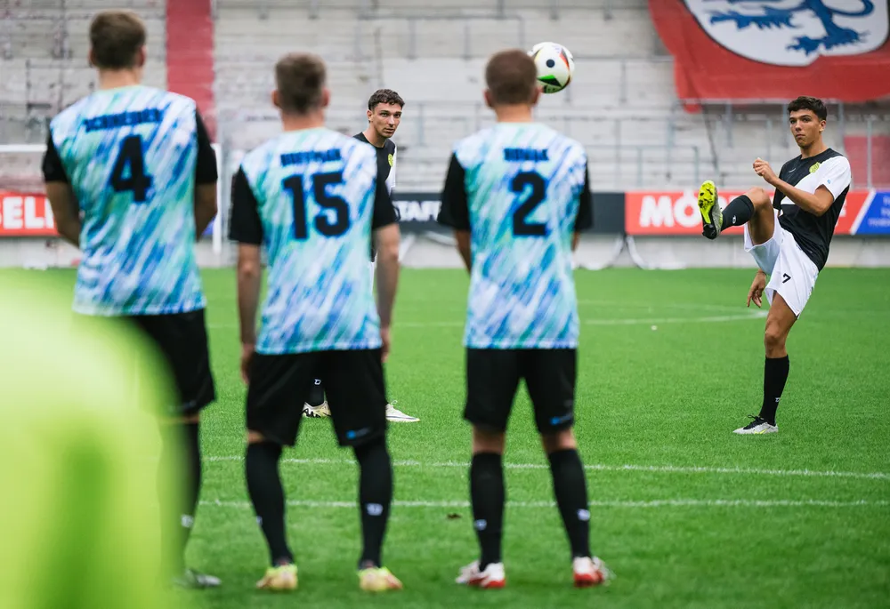 Un gruppo di calciatori in maglie colorate si trova in campo mentre un giocatore si prepara a battere un calcio di punizione.