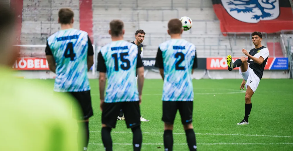 Un calciatore sta tirando mentre altri giocatori in maglie colorate guardano.