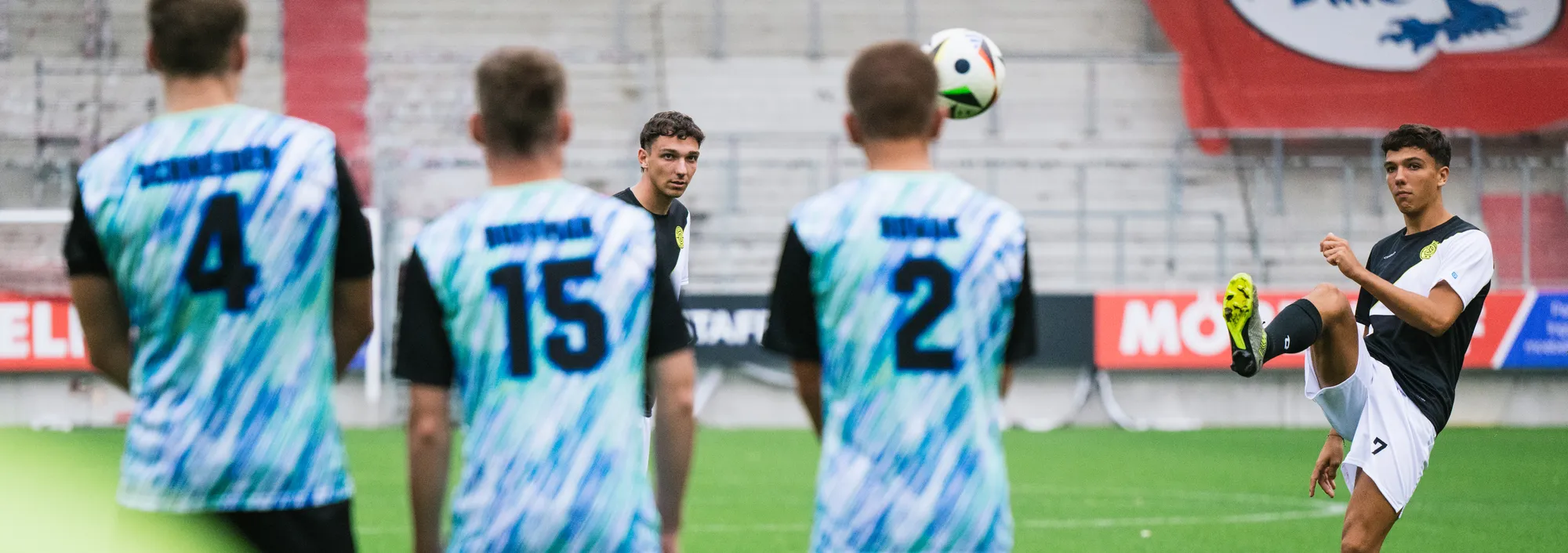 Un gruppo di calciatori in maglie colorate si trova sul campo mentre uno di loro solleva un pallone con il piede.