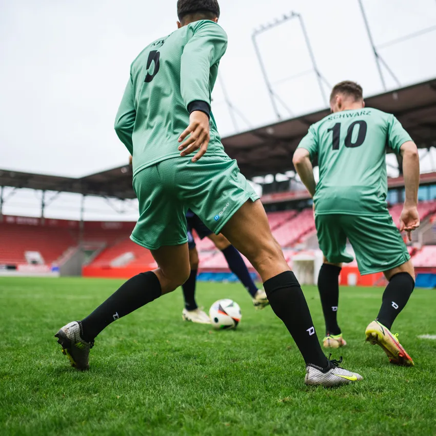 Due giocatori in magliette da calcio verdi e calze nere che giocano su un campo in uno stadio.