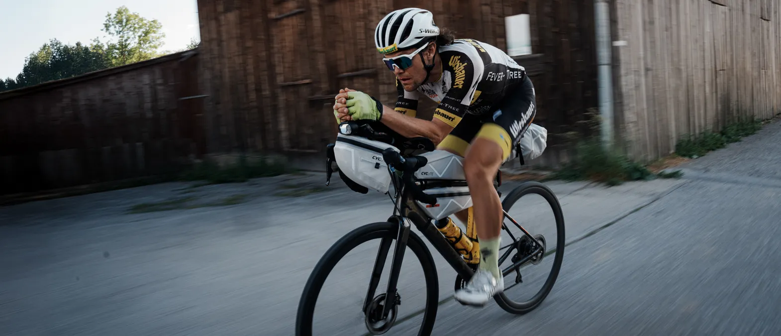Un ciclista in posizione aerodinamica su una bicicletta da strada, indossa abbigliamento sportivo personalizzato di owayo, mentre pedala su una strada.