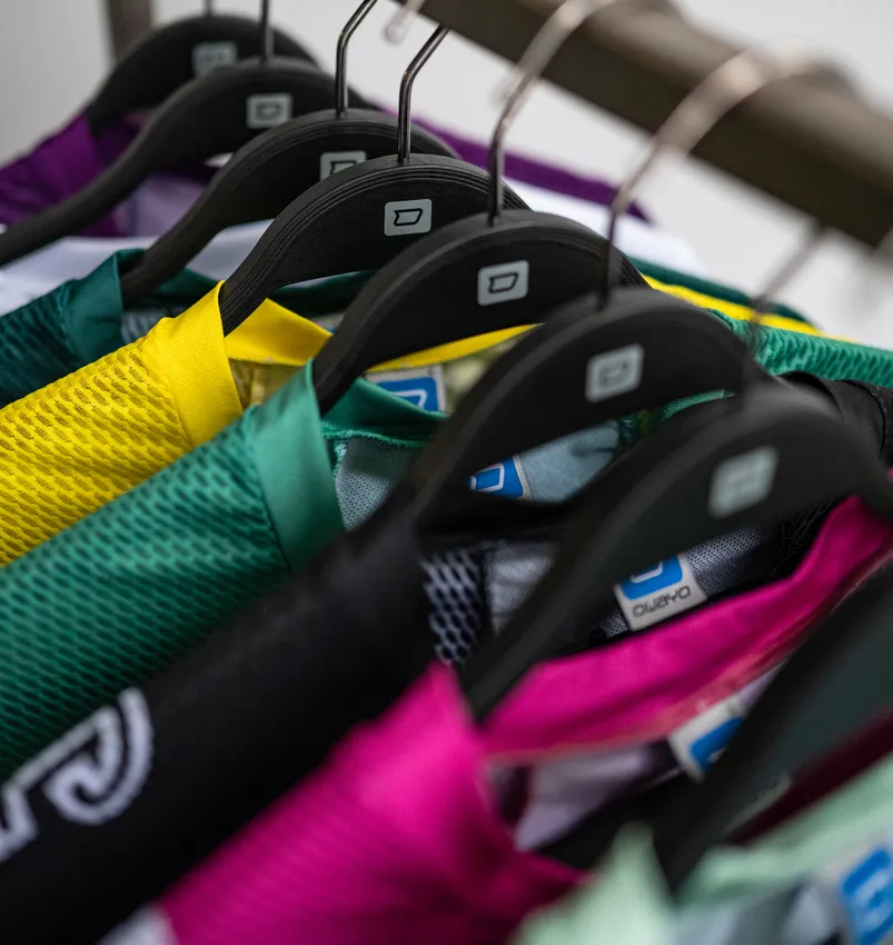Diversi capi di abbigliamento sportivo colorati su misura appesi a grucce nere.