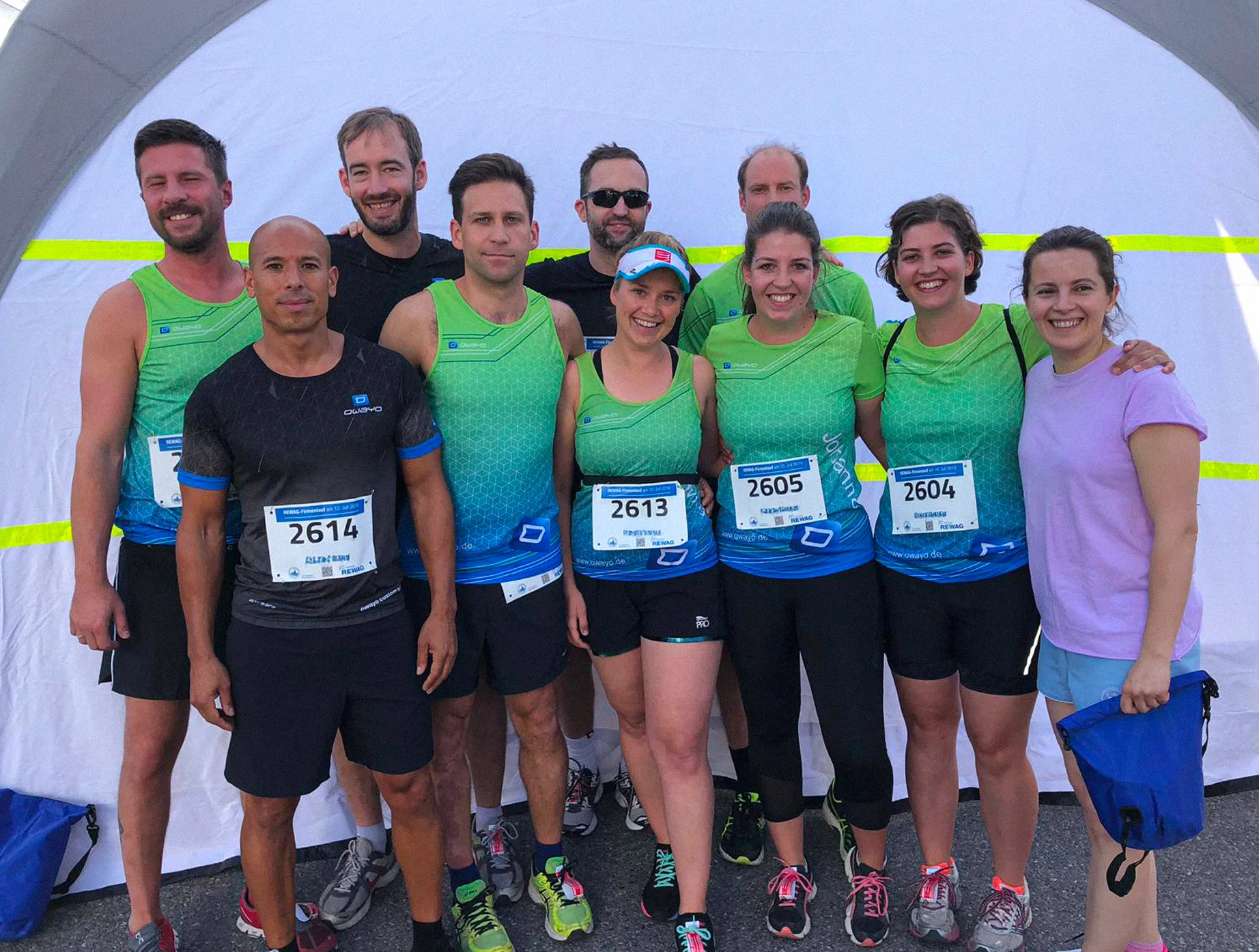 Un gruppo di corridori in abbigliamento sportivo personalizzato di owayo posa davanti a una tenda, alcuni con numeri di gara.
