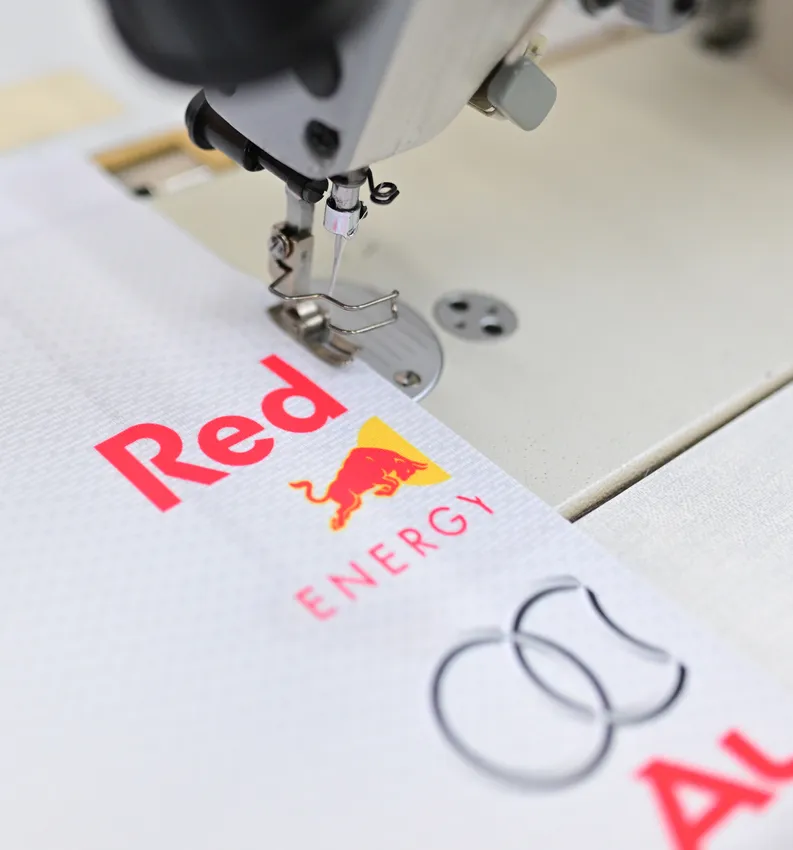 Una macchina da cucire sta cucendo un indumento sportivo bianco con il logo rosso Red Bull.