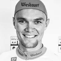 Un uomo con un abbigliamento da ciclismo con il logo 'Wiesbauer' sul berretto e la maglia.