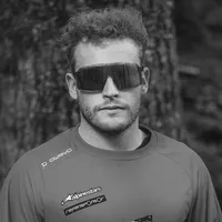 Un uomo con capelli ricci e occhiali da sole indossa una maglia sportiva grigia a maniche lunghe con il logo 'owayo' sulla spalla e altri loghi di sponsor sul petto.