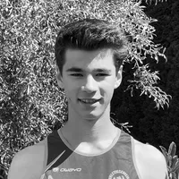 Un giovane uomo indossa una maglia da sport senza maniche nera e grigia con il logo 'owayo' sul petto, sorride davanti a uno sfondo di foglie verdi.