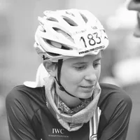 Una ciclista con una maglia da ciclismo nera con il logo 'IWC Schaffhausen', un casco bianco con il numero 183 e una sciarpa intorno al collo.