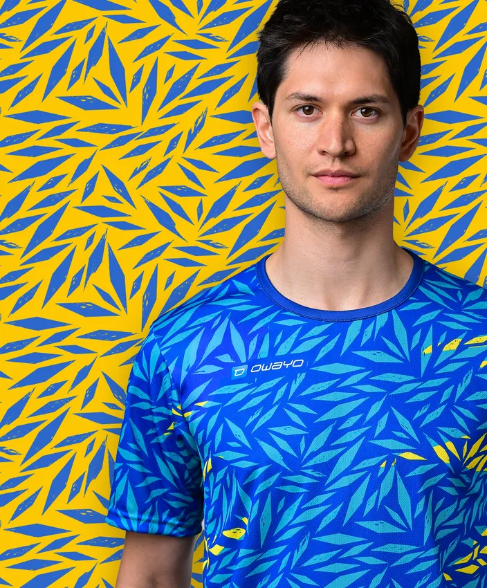 Un giovane indossa una maglietta sportiva blu con un motivo di foglie colorate su uno sfondo giallo.