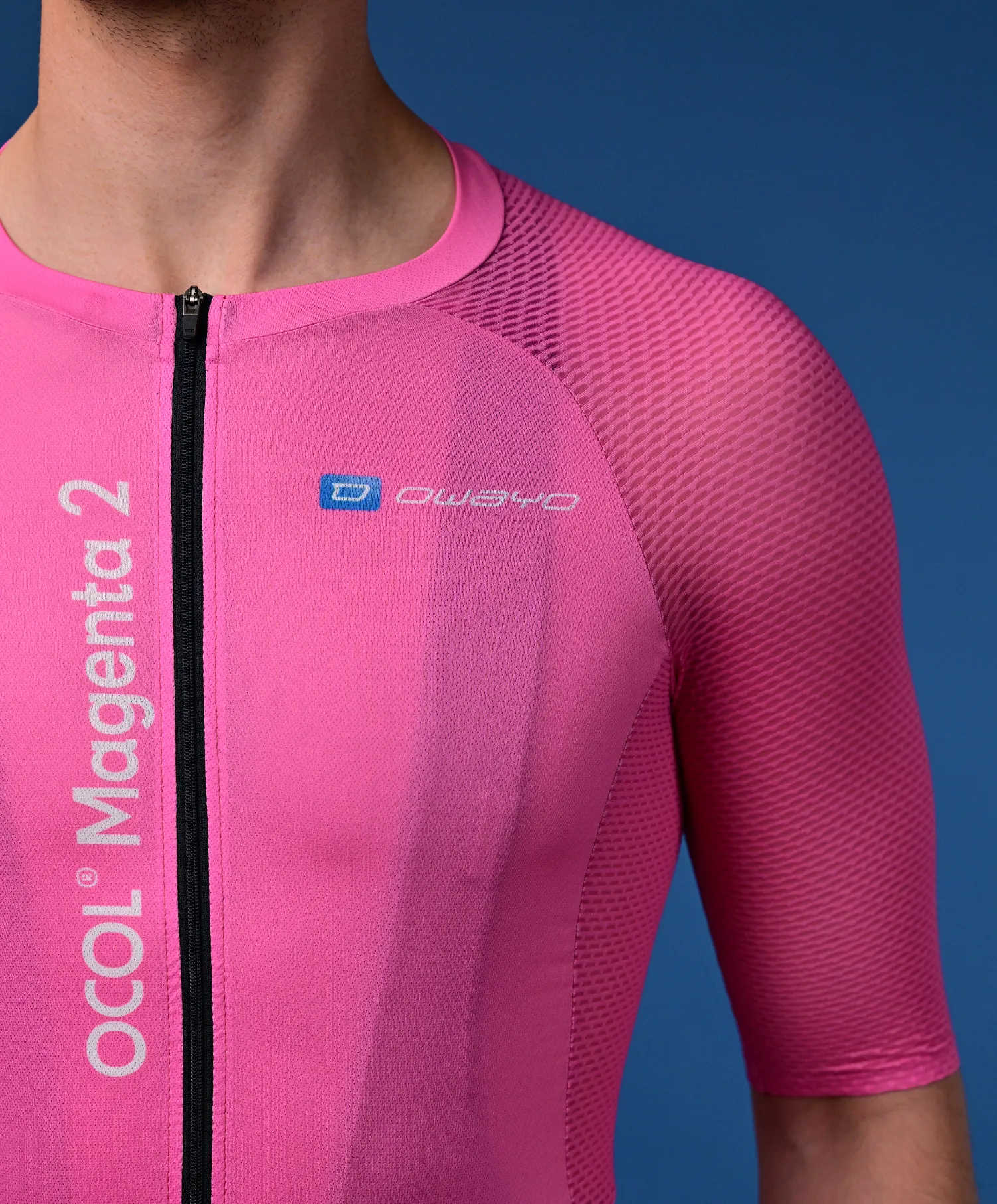 Un uomo indossa una maglia da ciclismo rosa a maniche corte con una cerniera nera e il logo 'owayo' sul petto. Sul lato sinistro è scritto verticalmente 'OCOL Magenta 2'.