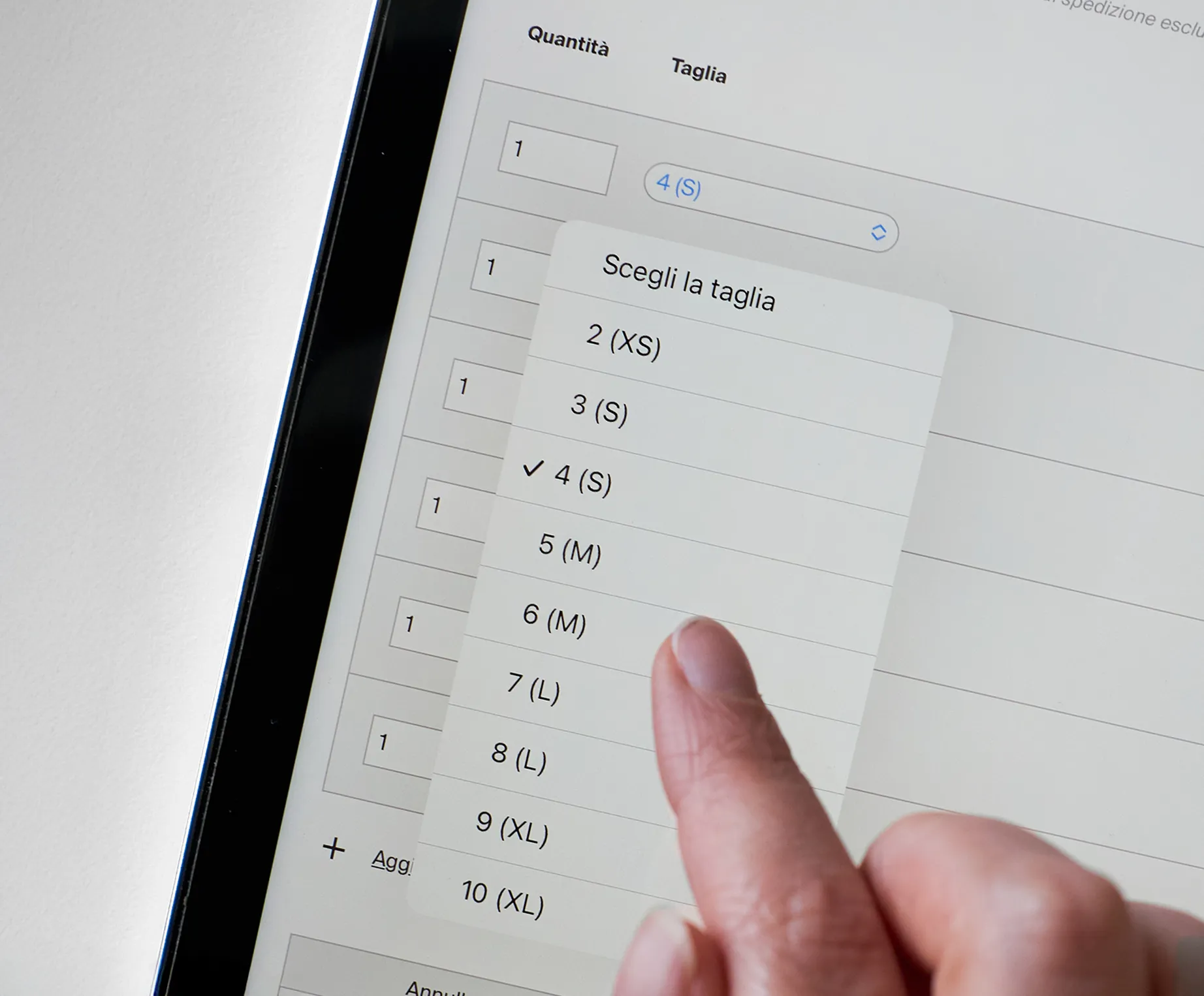 Un dito seleziona la taglia 4 (S) da una lista su un tablet che mostra una pagina di ordinazione di abbigliamento sportivo personalizzato.