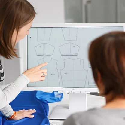 Due persone guardano modelli digitali di abbigliamento sportivo su uno schermo del computer, mentre una persona indica lo schermo.