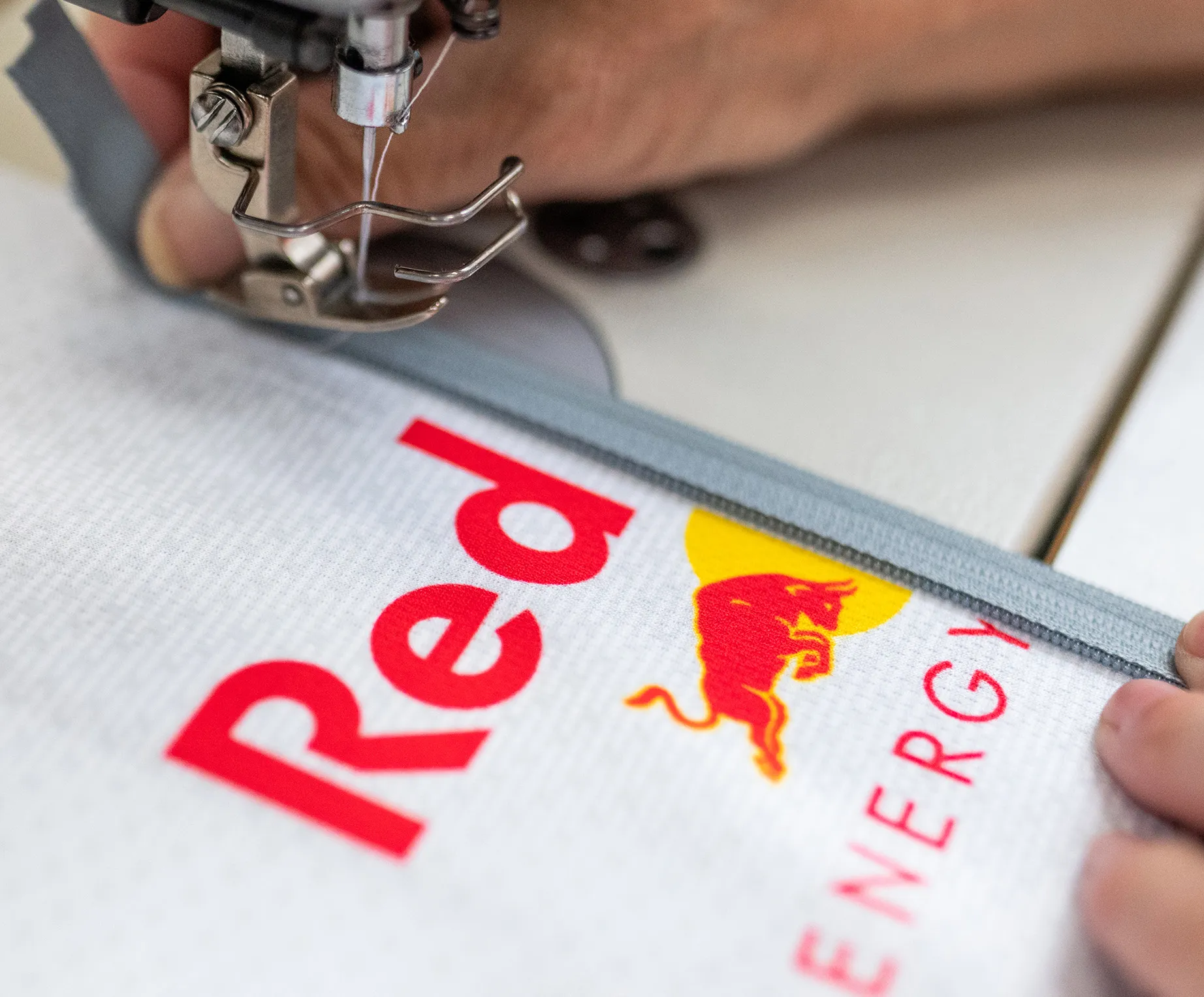 Una macchina da cucire sta cucendo una cerniera grigia su un indumento sportivo bianco con il logo Red Bull.