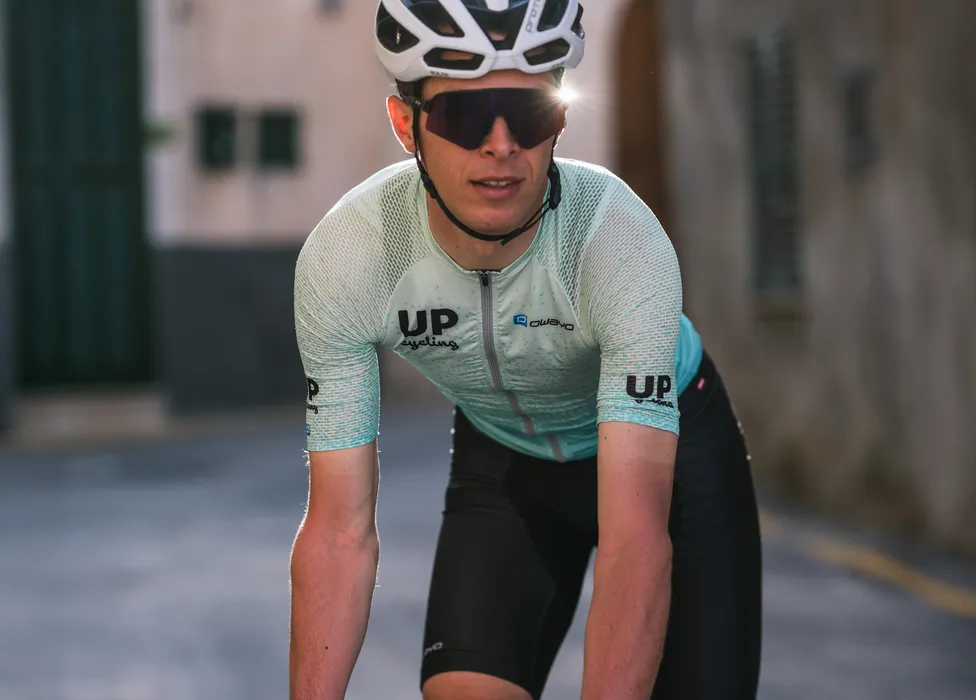 Un ciclista indossa una maglia da ciclismo azzurra traspirante con i loghi 'UP cycling' e 'owayo' sul petto, in una posa sportiva su una strada.