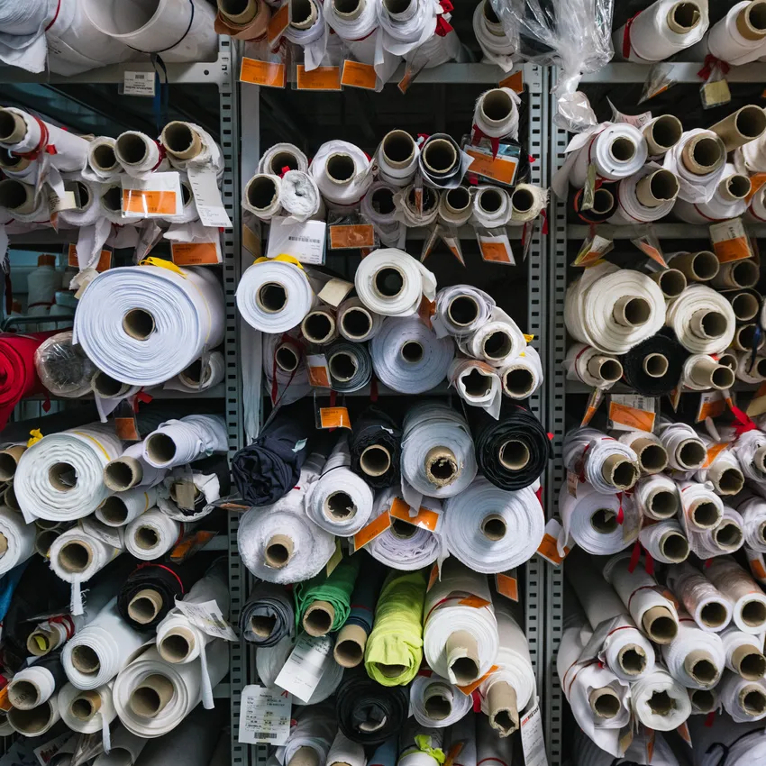 Scaffali pieni di rotoli di tessuto di vari colori e dimensioni, utilizzati per la produzione di abbigliamento sportivo.