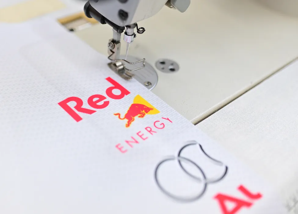 Una macchina da cucire sta cucendo un capo sportivo bianco con il logo rosso Red Bull Energy e un altro logo.